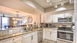Una cocina moderna con gabinetes blancos, electrodomésticos de acero inoxidable, encimeras de granito y una isla central con pileta.