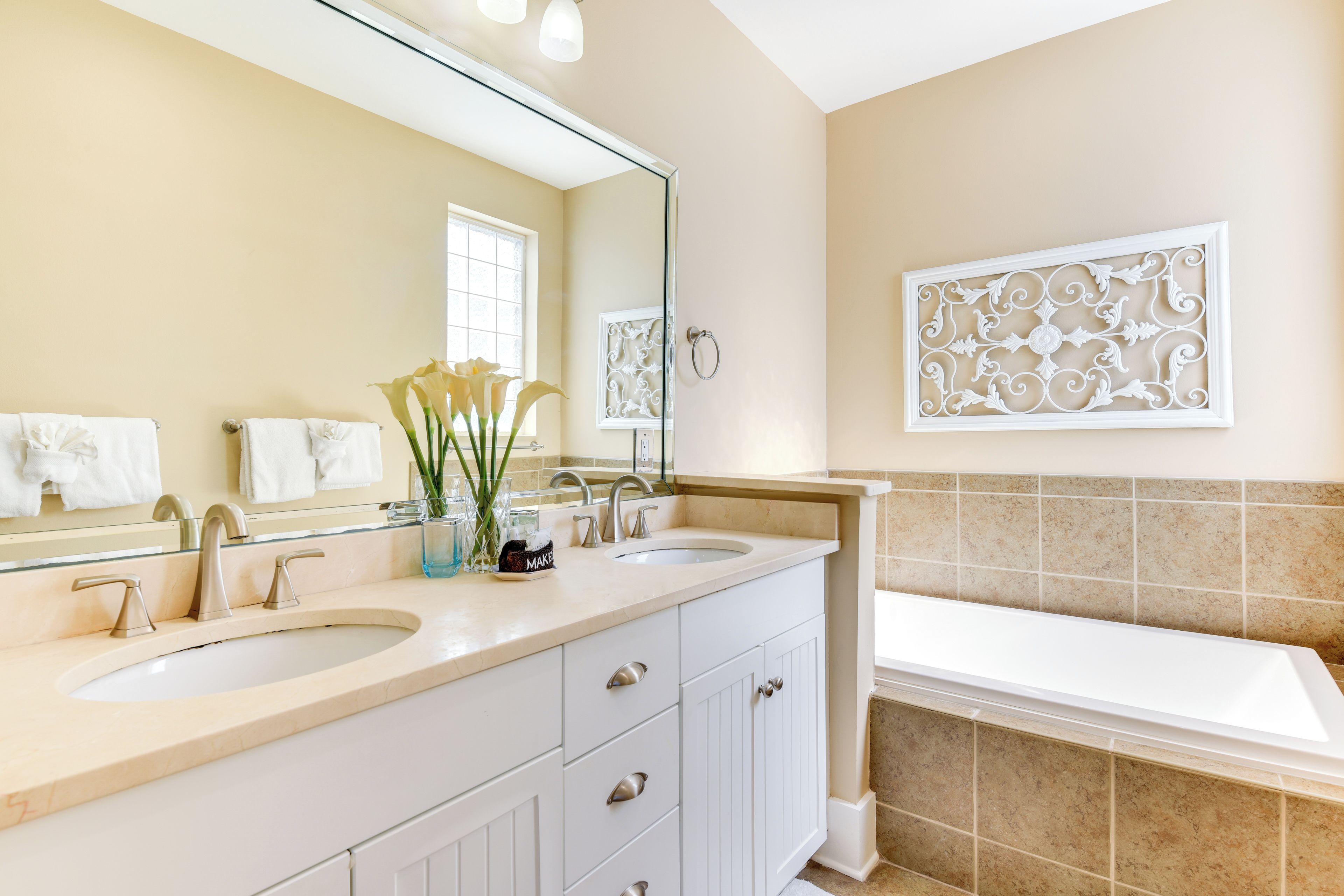 A bathroom with two sinks, a large mirror, a bathtub, and decorative wall art.