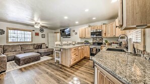 A spacious living room with a large sectional sofa, a wooden dining table, and a kitchen area with granite countertops and wooden cabinets. - Ruidoso Vacation Rental w/ Covered Hot Tub! (Ruidoso)