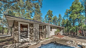 A two-story house with a brick exterior, a covered porch, and a small garden area with a fire pit. - Ruidoso Vacation Rental w/ Covered Hot Tub! (Ruidoso)