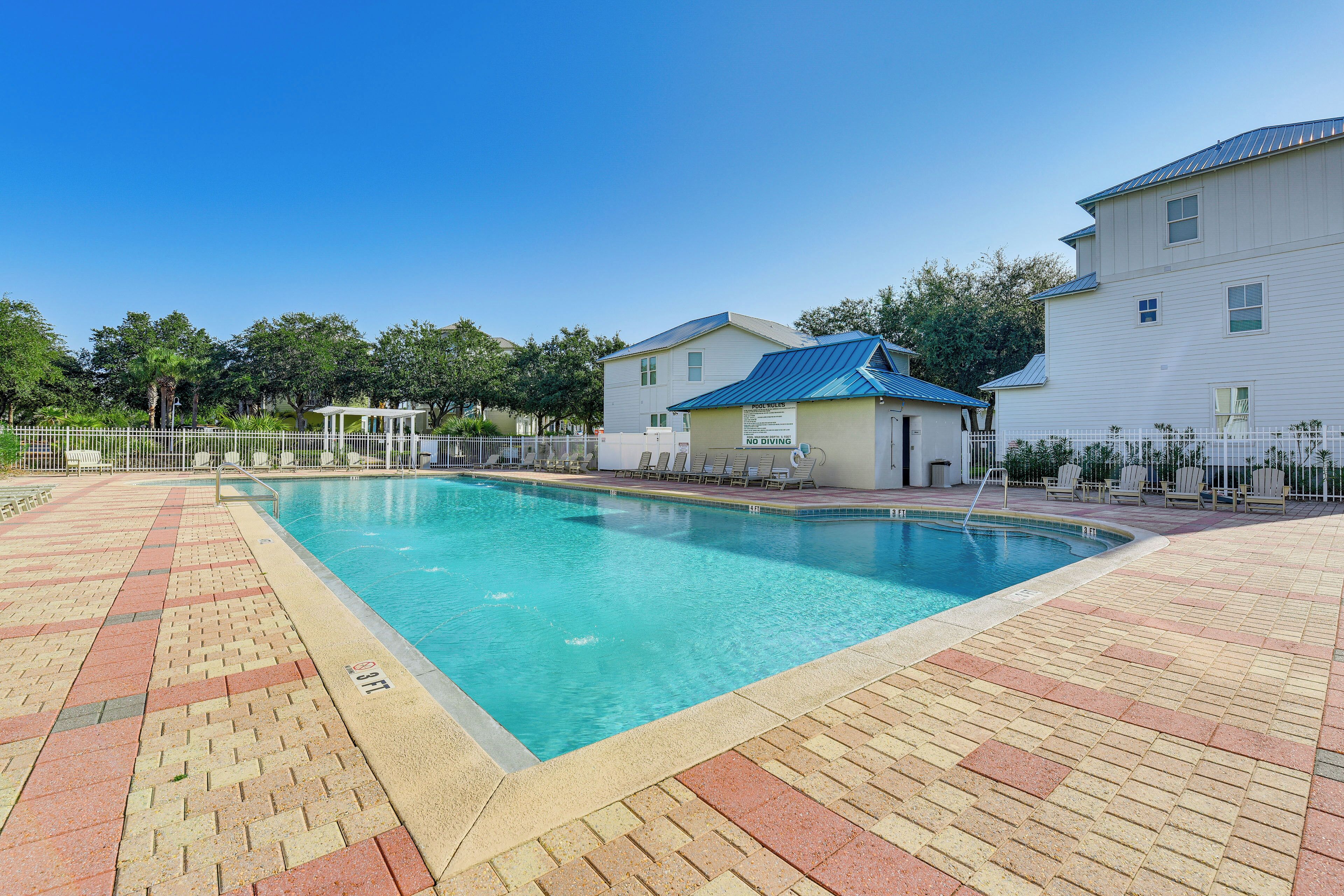 A swimming pool with a tiled deck, a covered area, and a building with a blue roof.