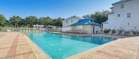 A swimming pool with a tiled deck, a covered area, and a building with a blue roof.