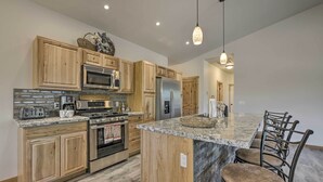 A modern kitchen with wooden cabinets, stainless steel appliances, granite countertops, and a bar area with bar stools.