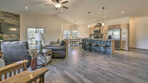 A spacious living room with a large gray sofa, a wooden coffee table, and a dining area with a kitchen in the background.