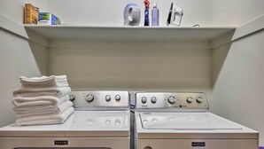 A laundry area with two Maytag washers and dryers, a stack of white towels, and cleaning supplies on a shelf.