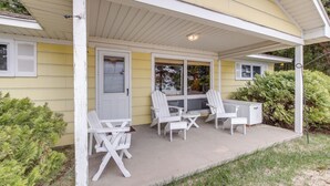 A covered porch with Adirondack chairs and a small table, a door, and a window with shutters. - Cozy Baileys Harbor Cottage on Lake Michigan! (Baileys Harbor)