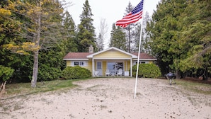 A house with a porch, a flag, and a grill in the yard. - Cozy Baileys Harbor Cottage on Lake Michigan! (Baileys Harbor)