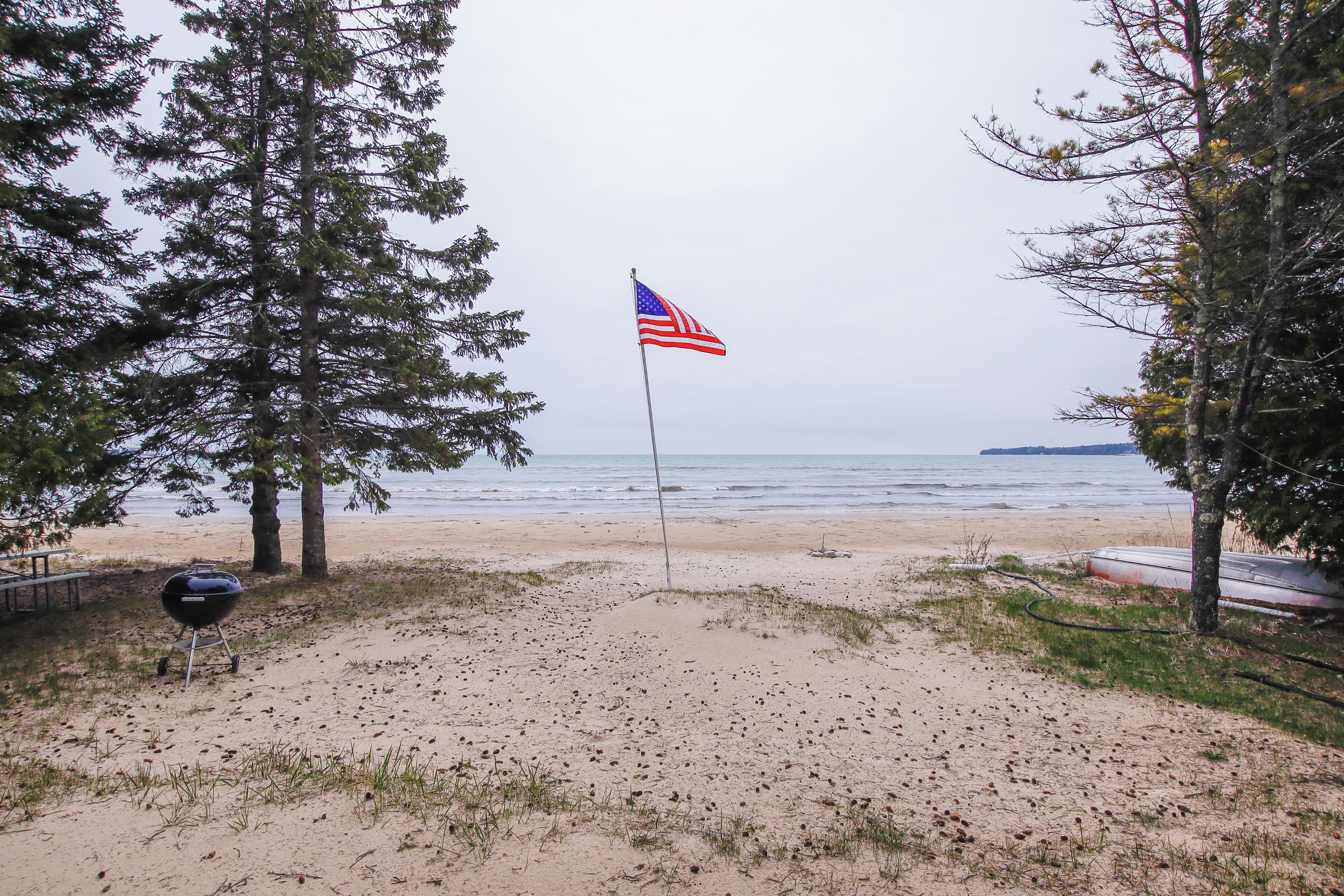 A beach with a flag, a grill, and a body of water.