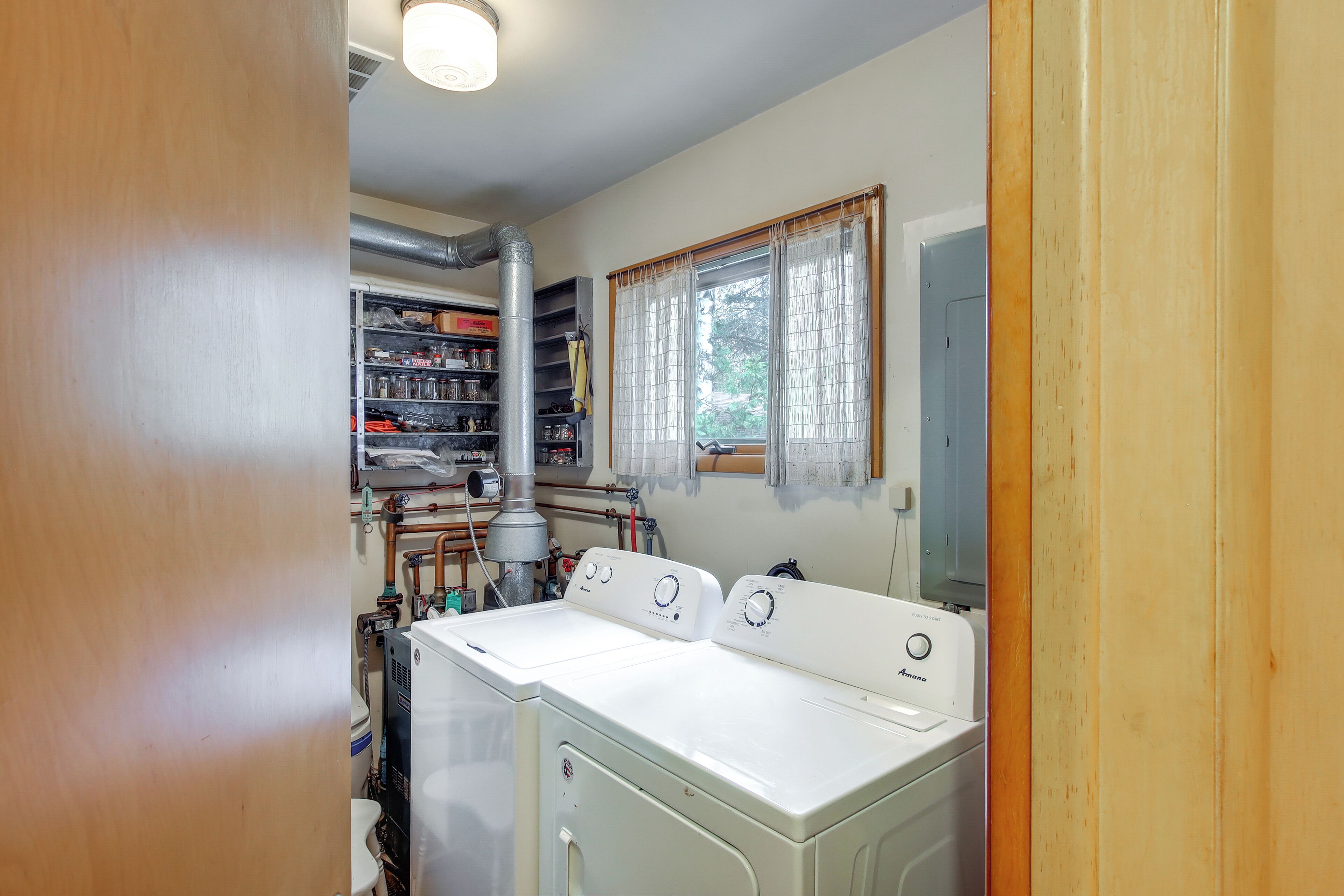 A laundry room with stacked shelves, a window with curtains, and a washing machine.