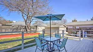 A deck with a glass table and chairs, a blue umbrella, and a view of a backyard and neighboring houses.