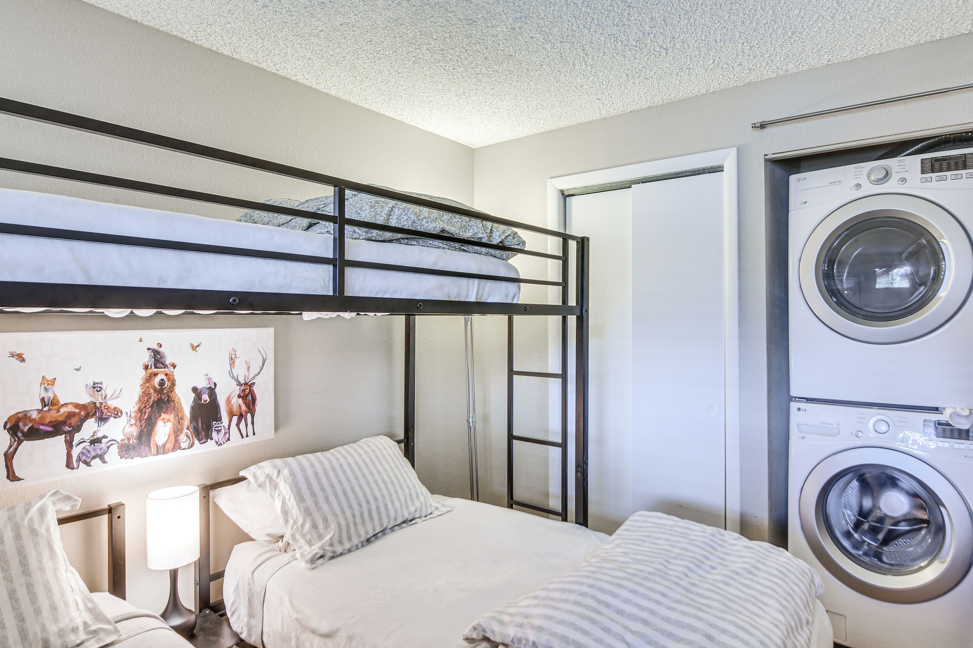 A bunk bed with a mural, a washing machine, and a bedside table with a lamp.