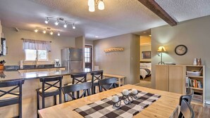 Une cuisine moderne dotée d’un îlot central, un coin repas avec une table et des chaises en bois, et un espace de vie chaleureux avec un lit et une bibliothèque.