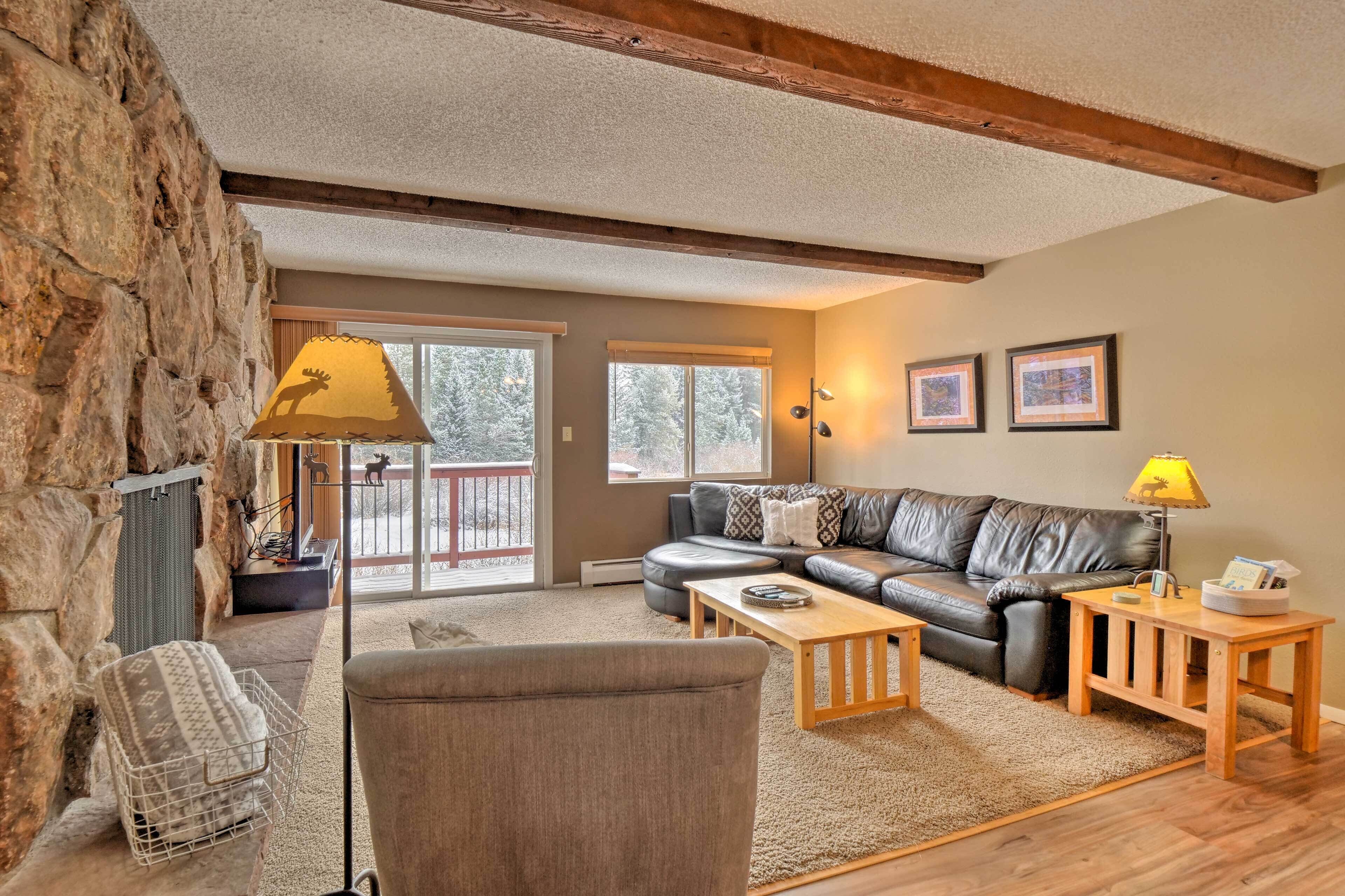 A cozy living room with a stone wall, a leather sofa, a wooden coffee table, and a fireplace.