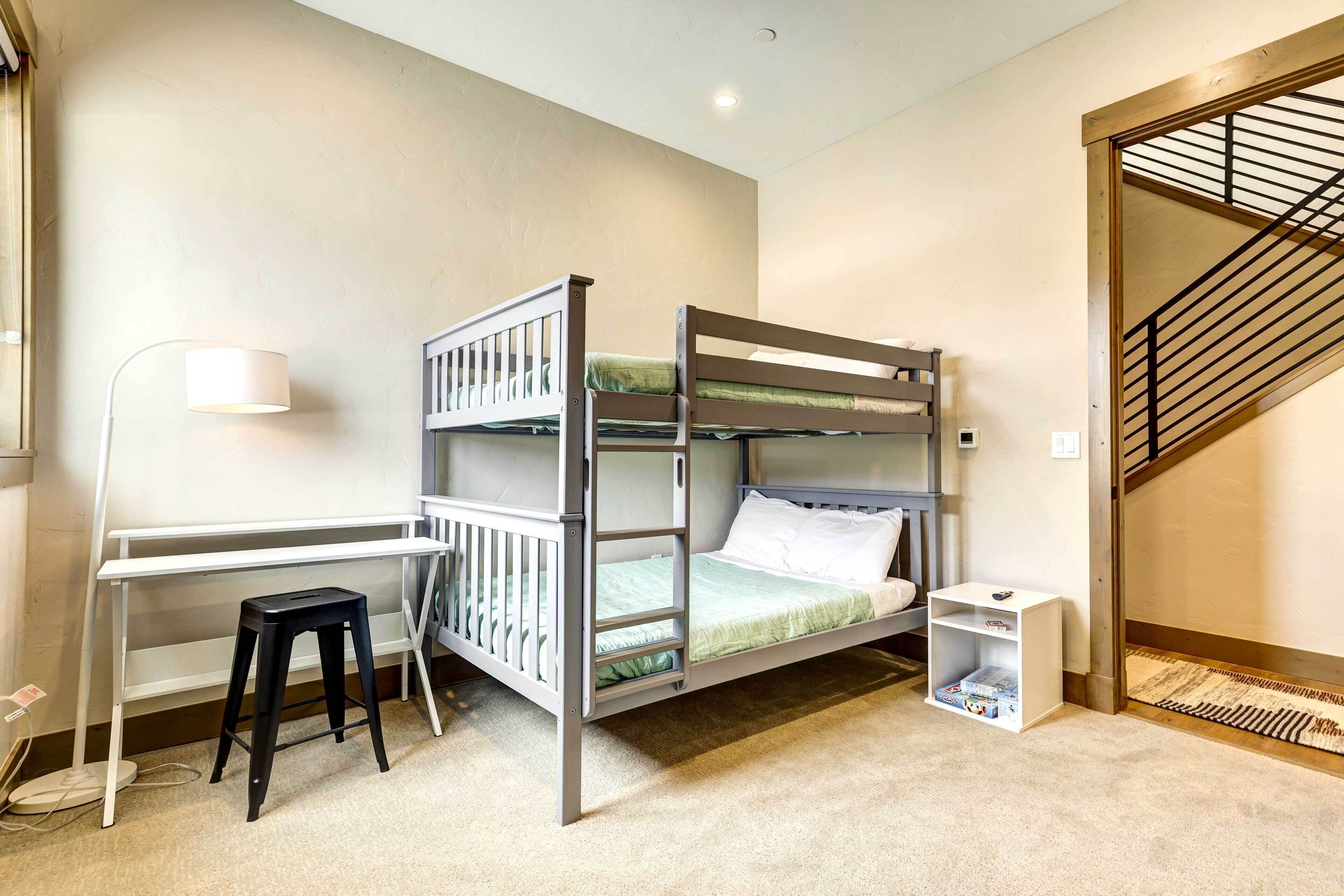 A bunk bed with a desk and chair, a small stool, and a bookshelf.