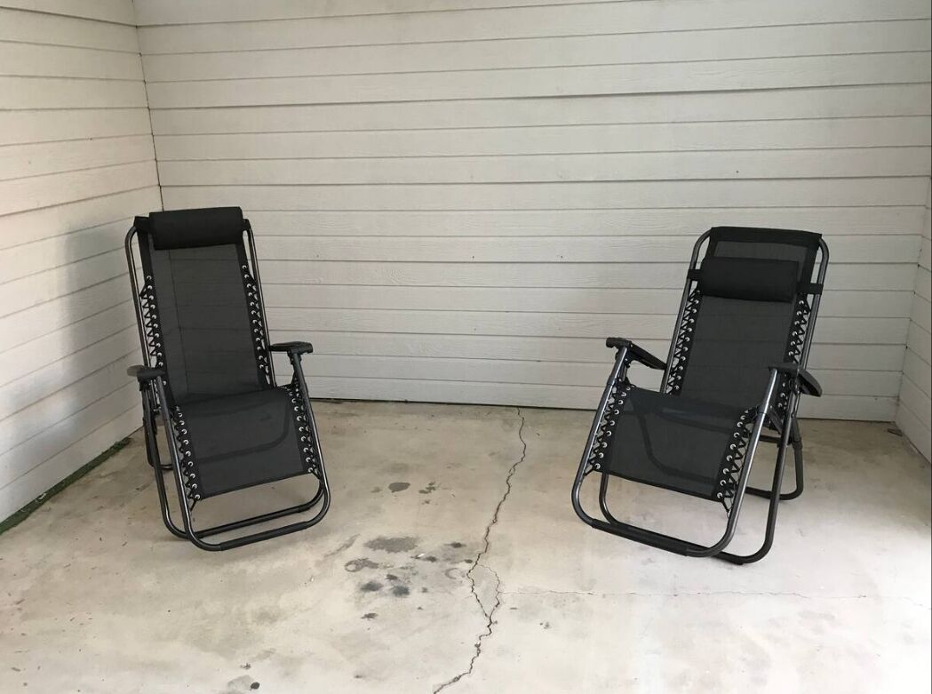 Two black metal chairs with mesh backs and armrests, positioned on a concrete floor with visible cracks.