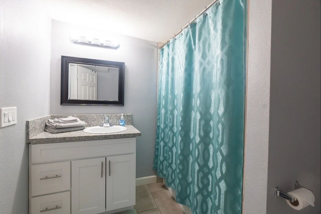 Une salle de bain avec un lavabo, un miroir et un rideau de douche.