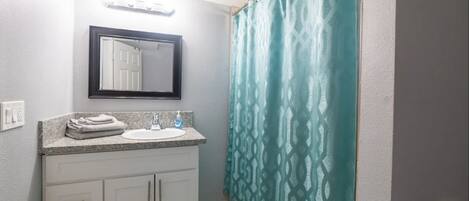 Une salle de bain avec un lavabo, un miroir et un rideau de douche.