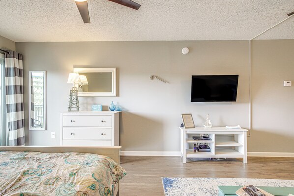 Quarto com cama, penteadeira, televisão e uma mesinha com objetos decorativos.