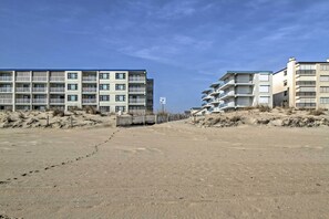 Um hotel na praia com várias varandas, uma praia arenosa em frente e um céu claro.