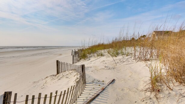 Une plage de sable avec une clôture en bois et de l’herbe.
