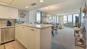 A modern kitchen with white cabinets, a central island, and a dining area with a sofa and chairs. - St Augustine Condo w/ Direct Ocean Access! (St. Augustine)