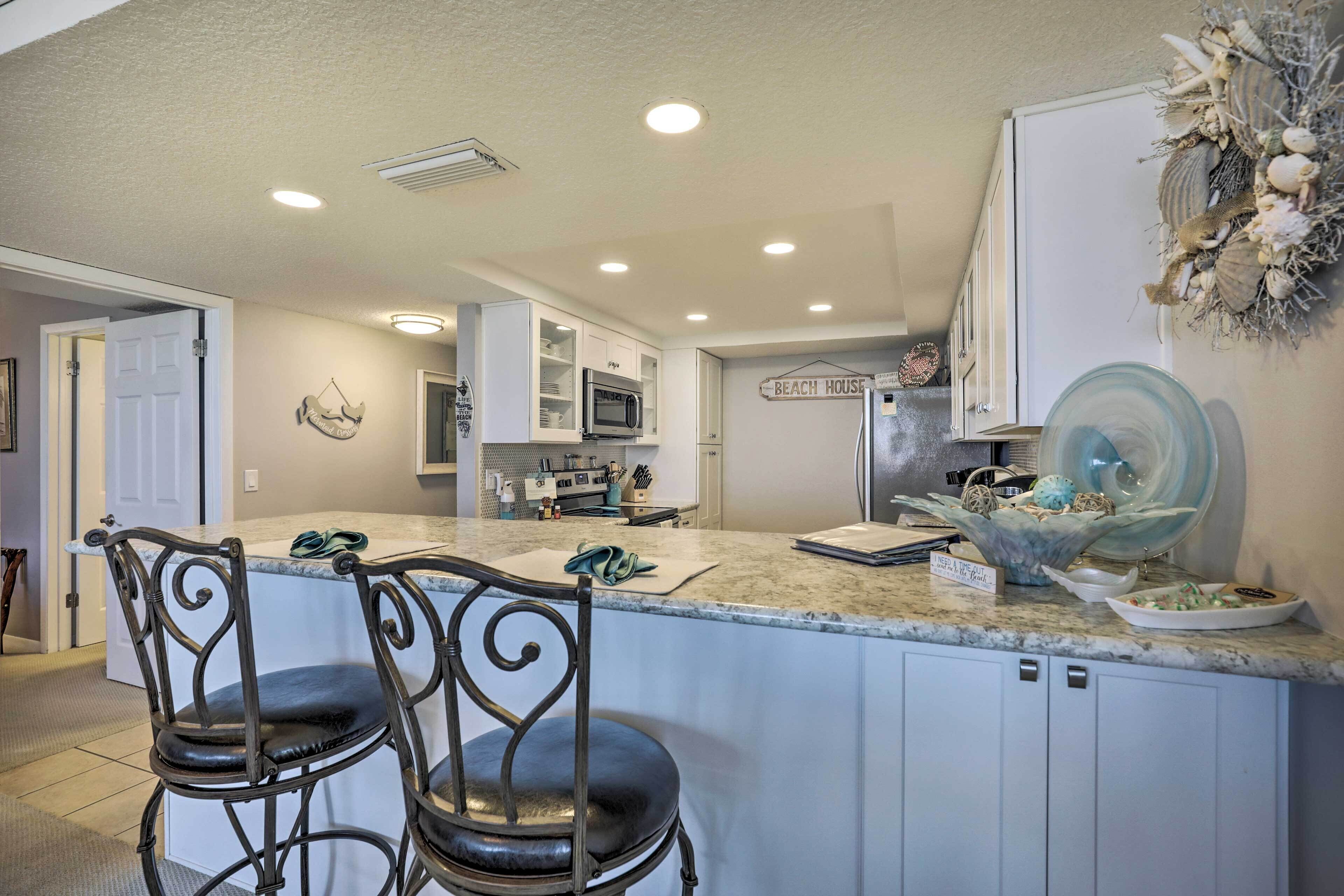 A kitchen with a central island, bar stools, white cabinets, and a decorative wall piece.