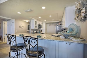 A kitchen with a central island, bar stools, white cabinets, and a decorative wall piece. - St Augustine Condo w/ Direct Ocean Access! (St. Augustine)