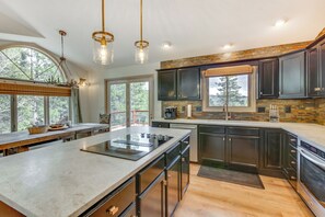 A modern kitchen with a large island, dark cabinetry, and a stone backsplash. - Angel Fire Rental Cabin w/ Hot Tub & Mountain View (Angel Fire)