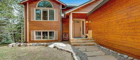 A wooden cabin with a stone pathway leading to the entrance, surrounded by a natural landscape.
