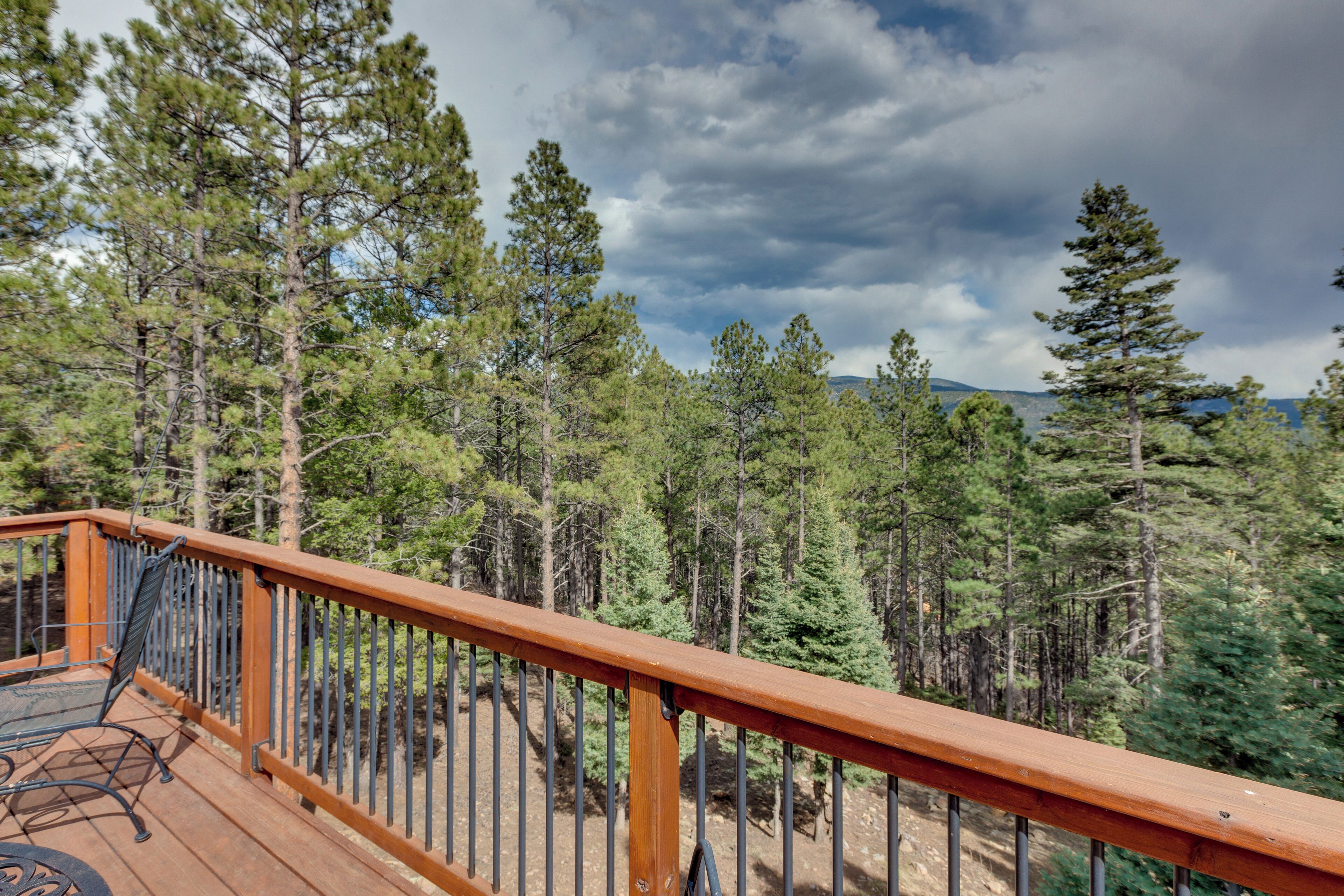 A wooden deck with a metal railing overlooking a forested area with tall pine trees.