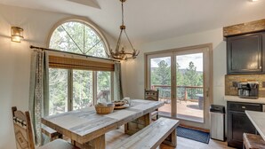 A spacious kitchen with a large wooden table, a chandelier, and a view of the outdoors through a large window. - Angel Fire Rental Cabin w/ Hot Tub & Mountain View (Angel Fire)