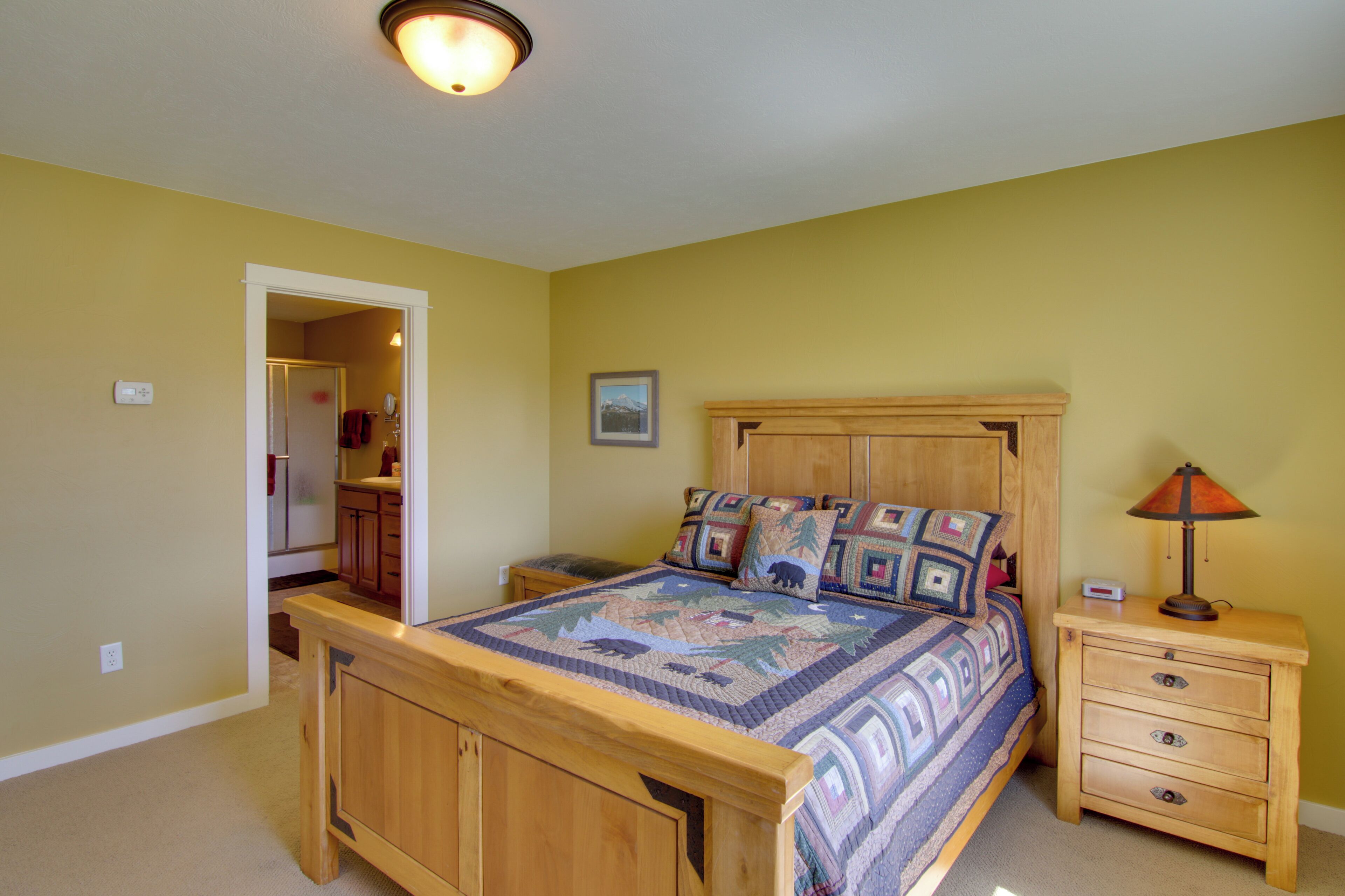 Een slaapkamer met een houten bed, een nachtkastje met lades, een lamp en een deur naar een badkamer.