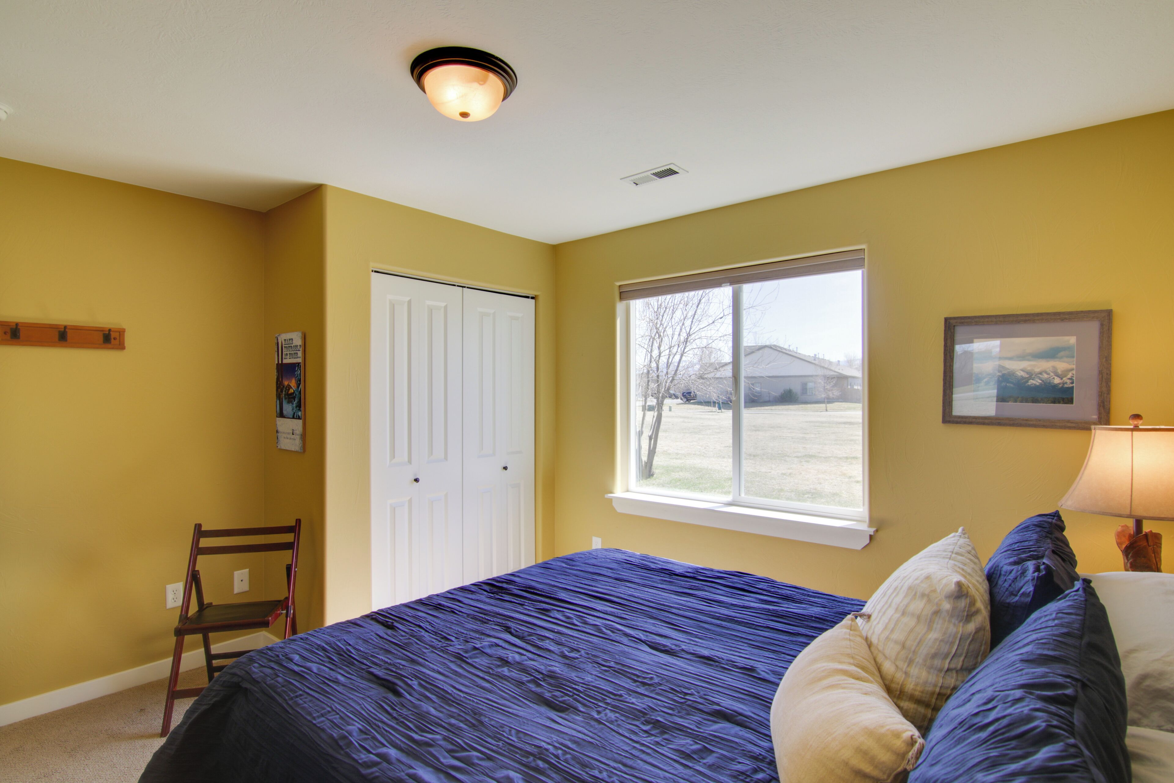 A bedroom with a bed, a window, a chair, and a door.