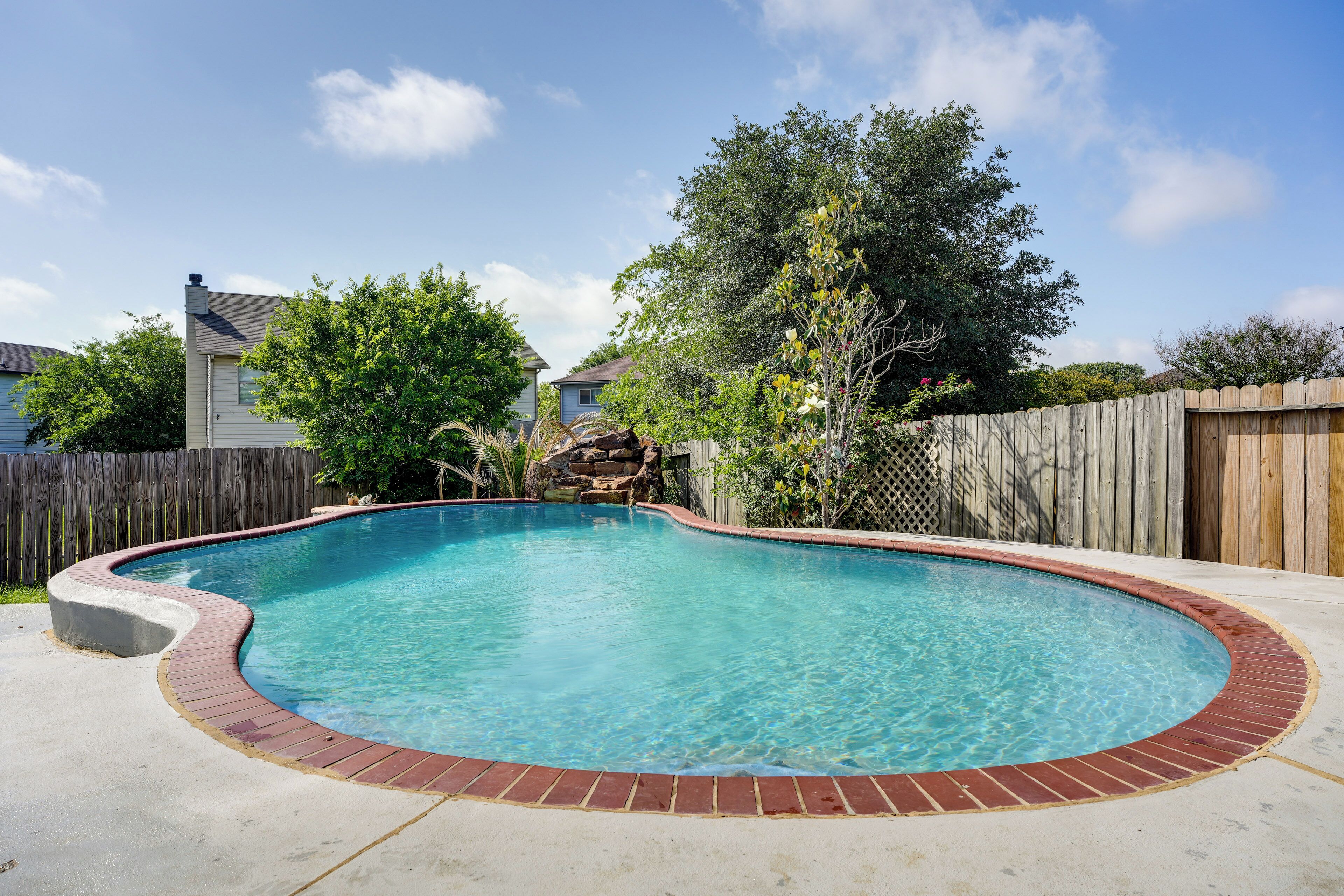 A backyard with a swimming pool, a wooden fence, and a house in the background.