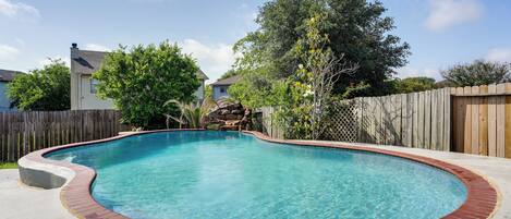 A backyard with a swimming pool, a wooden fence, and a house in the background.