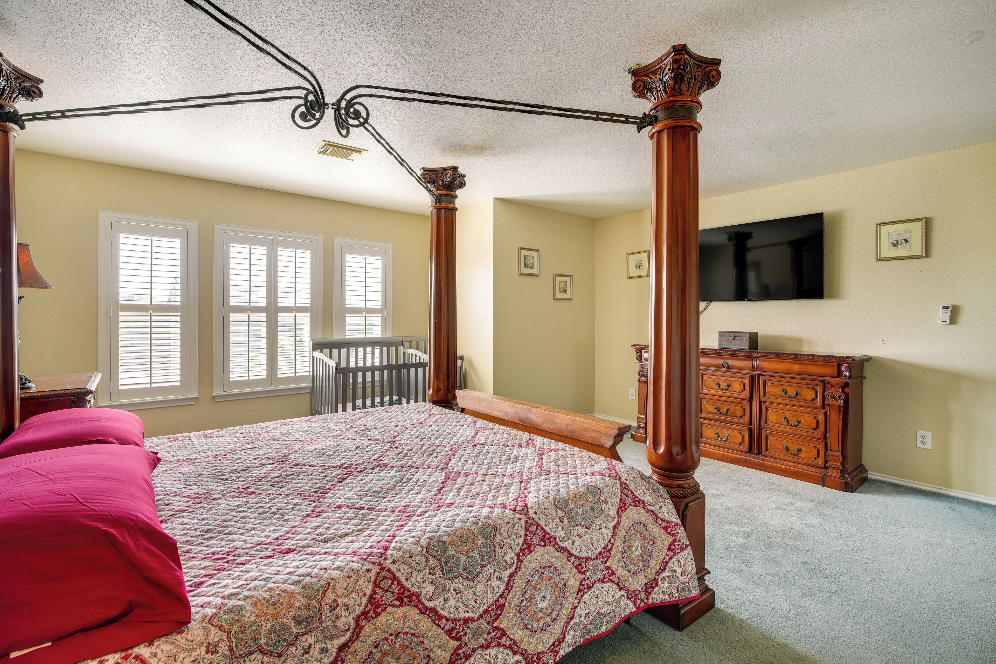 A bedroom with a four-poster bed, a wooden dresser, and a television on the wall.