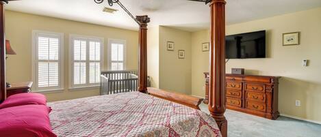 A bedroom with a four-poster bed, a wooden dresser, and a television on the wall.