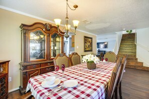 Une salle à manger avec une nappe à carreaux, des chaises en bois, un lustre et un grand miroir.