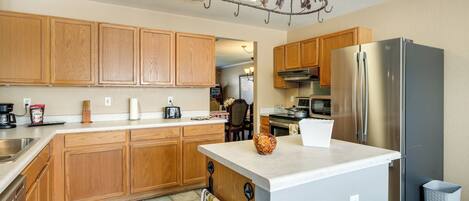 A kitchen with wooden cabinets, a stainless steel refrigerator, a white countertop, and a patterned rug.