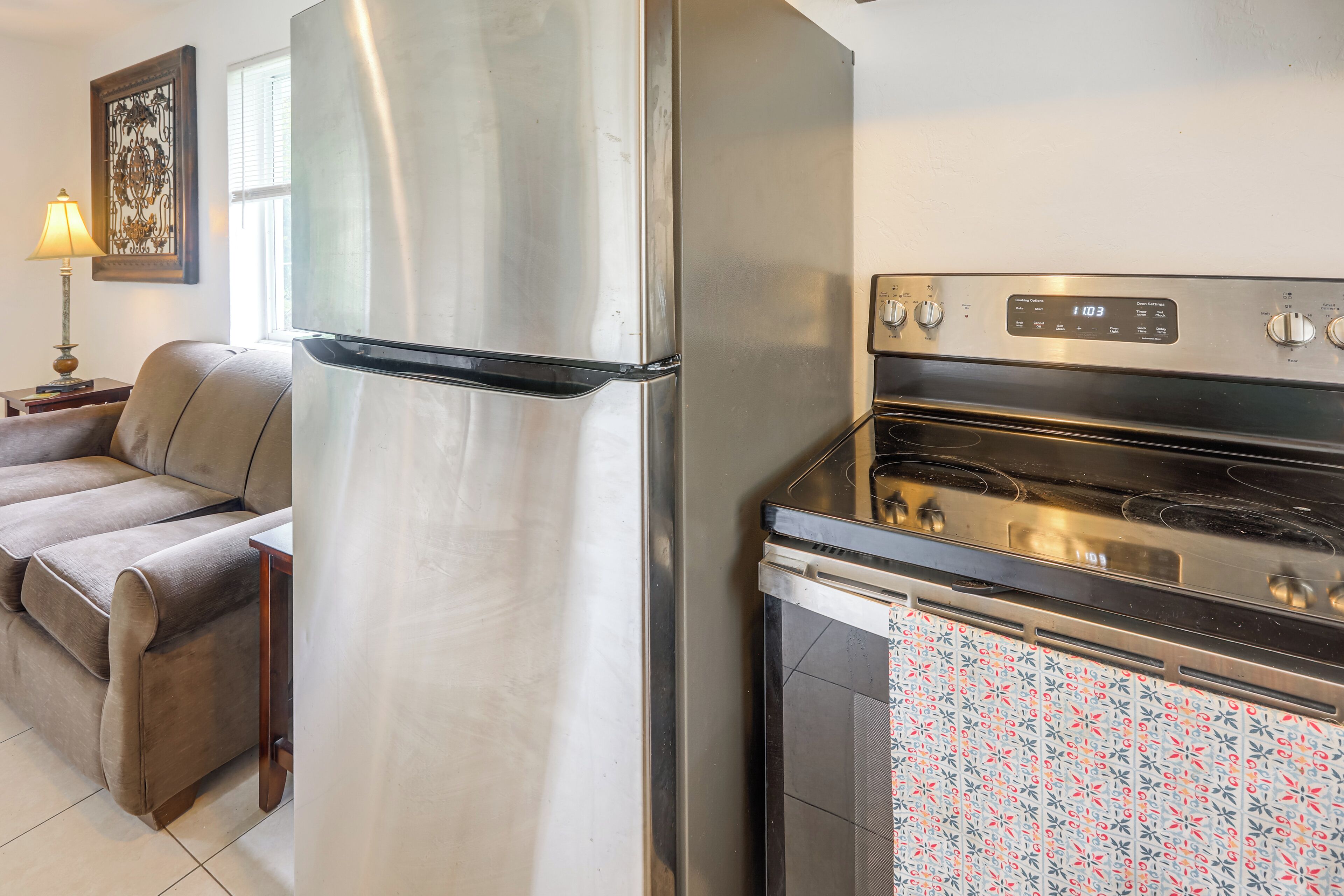 A kitchen with a stainless steel refrigerator, an oven, and a patterned oven mitt hanging on the oven door.