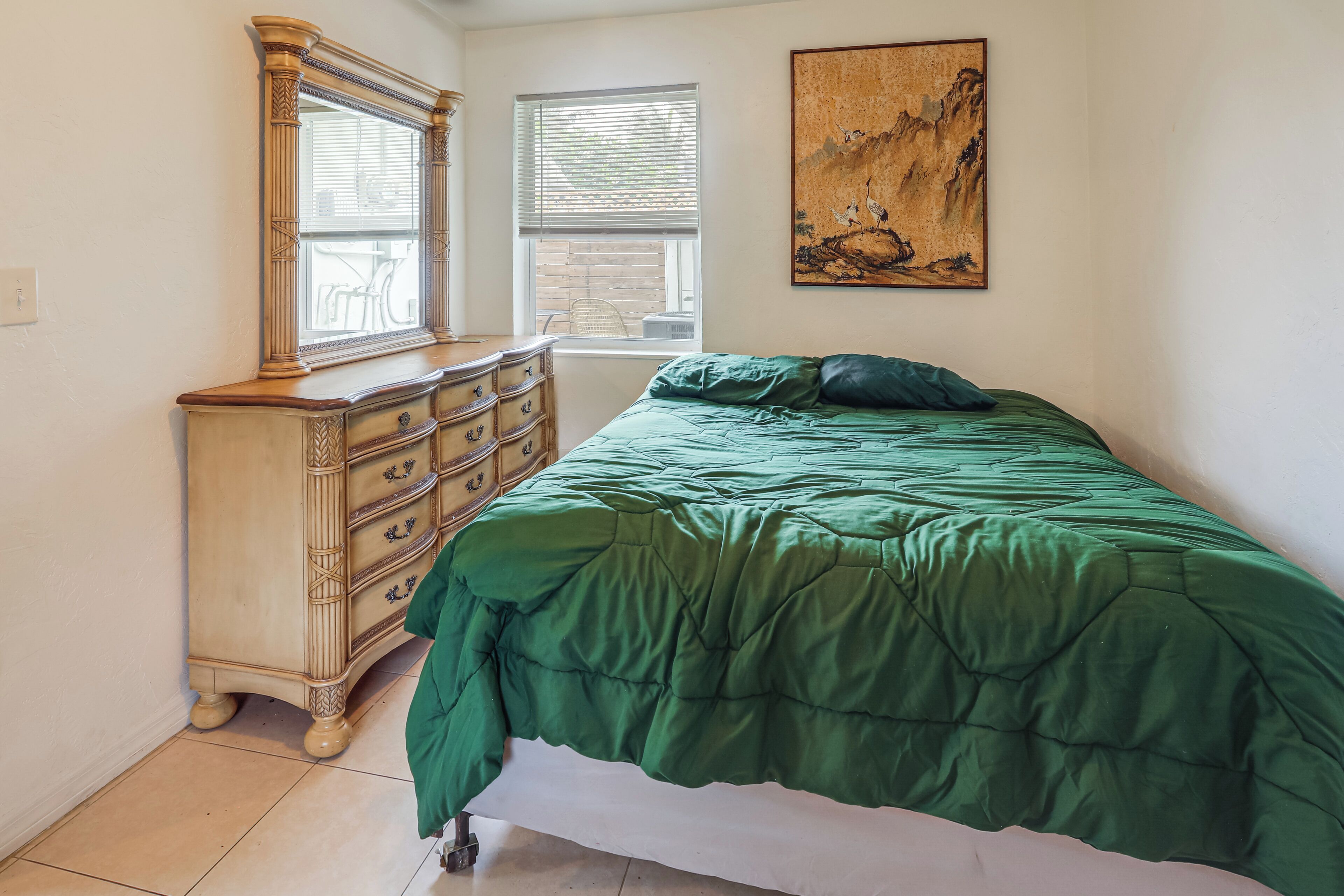 Un dormitorio con cama, cómoda, ventanas y un cuadro.