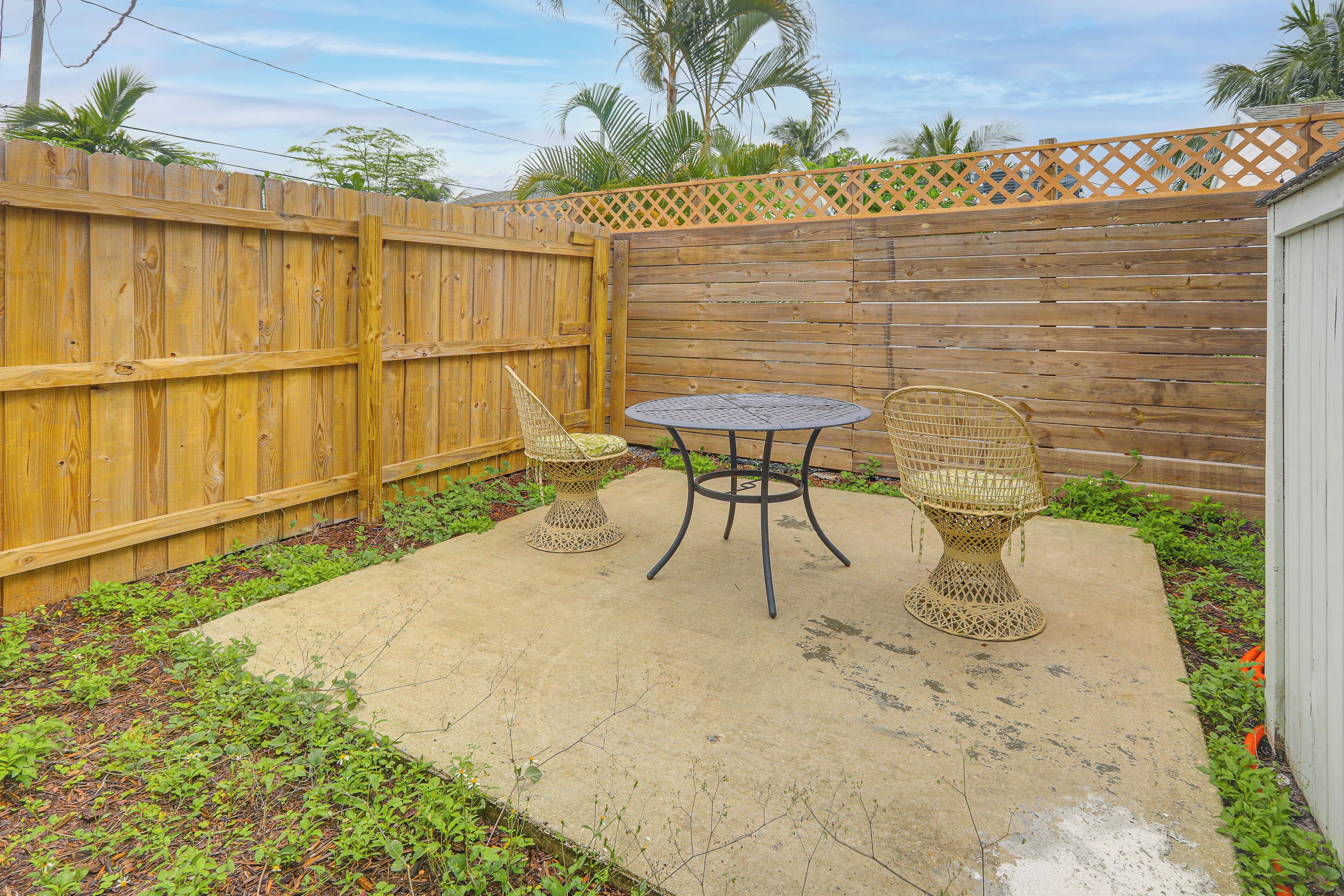 A patio with a wooden fence, two wicker chairs, and a round table.