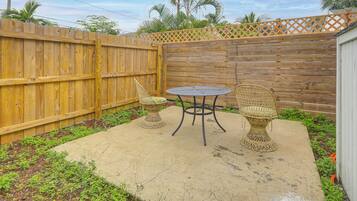 A patio with a wooden fence, two wicker chairs, and a round table.