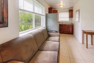 Una sala de estar con sofá, una mesita, un área de cocina con armarios y una ventana con persianas.