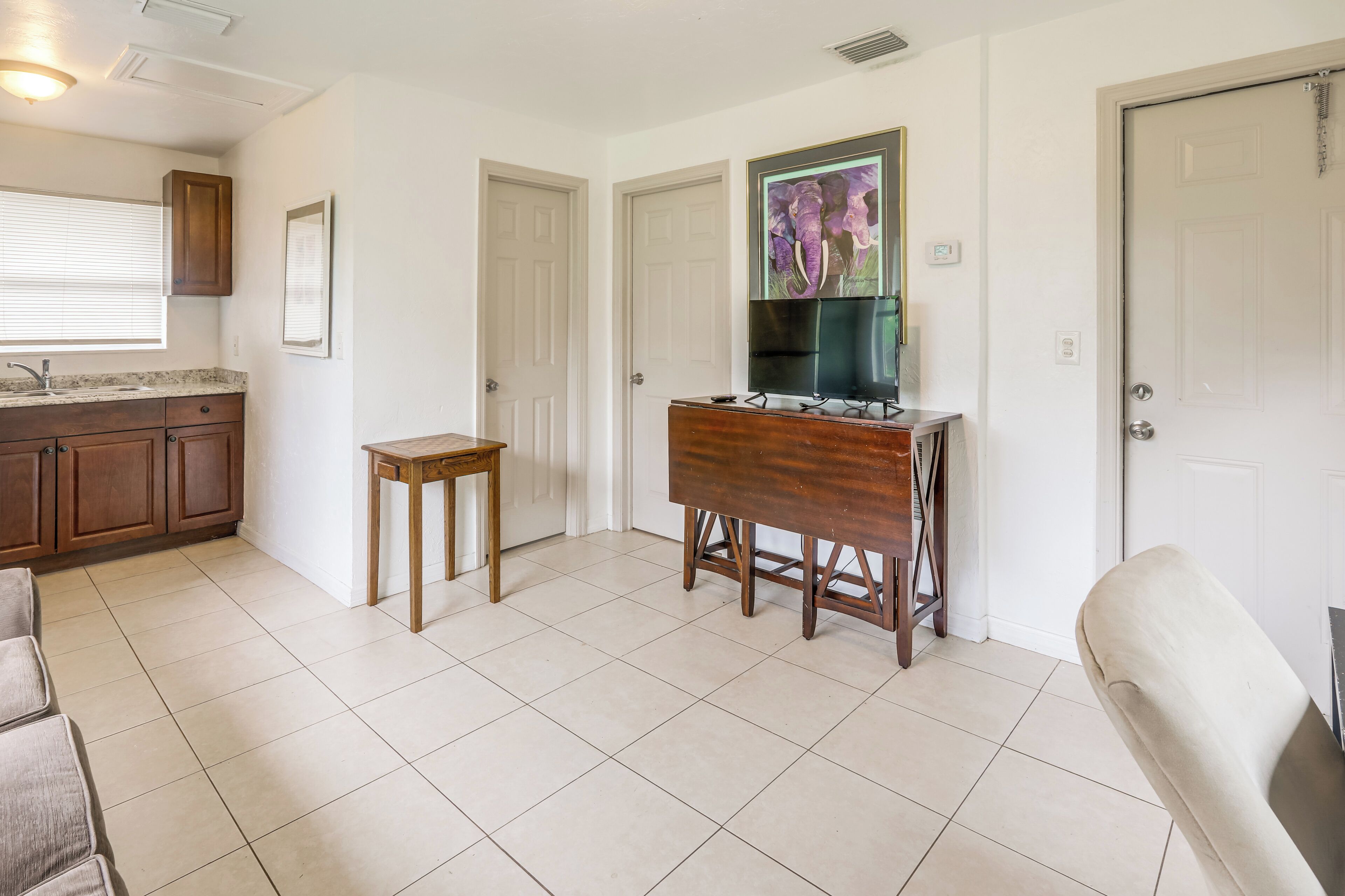 Una habitación con área de cocina, una mesa de comedor con sillas, un televisor montado en la pared y una puerta.
