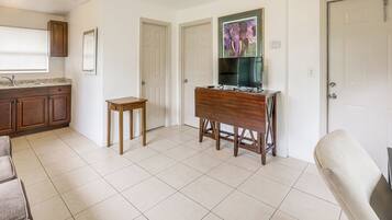 Una habitación con área de cocina, una mesa de comedor con sillas, un televisor montado en la pared y una puerta.