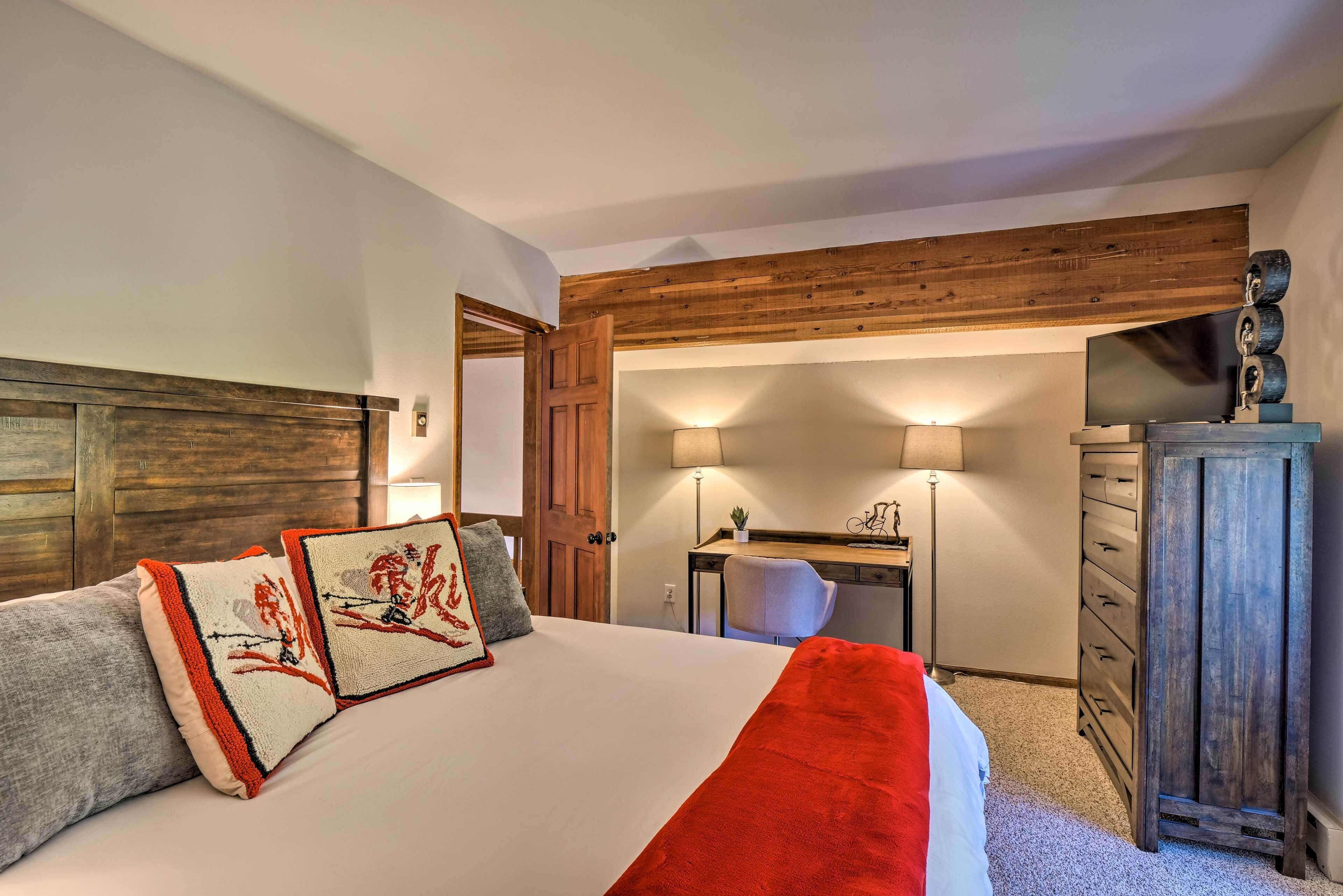 A bedroom with a wooden headboard, a bed with decorative pillows, a desk with a chair, a dresser, and a television.
