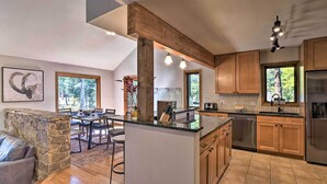 A spacious kitchen with wooden cabinets, a central island, and a dining area with a stone fireplace. - 6 Mi to Breck Resort: Family Cabin w/ Game Room (Breckenridge)