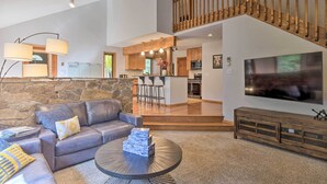 A spacious living area with a leather sofa, a coffee table, and a stone wall. A kitchen and dining area are visible in the background. - 6 Mi to Breck Resort: Family Cabin w/ Game Room (Breckenridge)