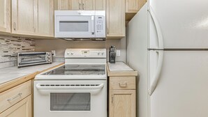 Una cocina compacta con armarios de madera, microondas, tostadora, estufa y refrigerador.